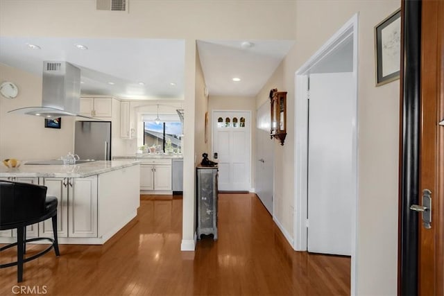 kitchen with a breakfast bar, white cabinetry, island range hood, appliances with stainless steel finishes, and dark hardwood / wood-style flooring