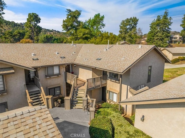 multi unit property featuring a shingled roof, stairway, and stucco siding