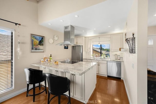 kitchen with white cabinetry, stainless steel appliances, a kitchen breakfast bar, island range hood, and kitchen peninsula