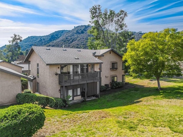 rear view of house featuring central AC unit, a balcony, a mountain view, and a lawn