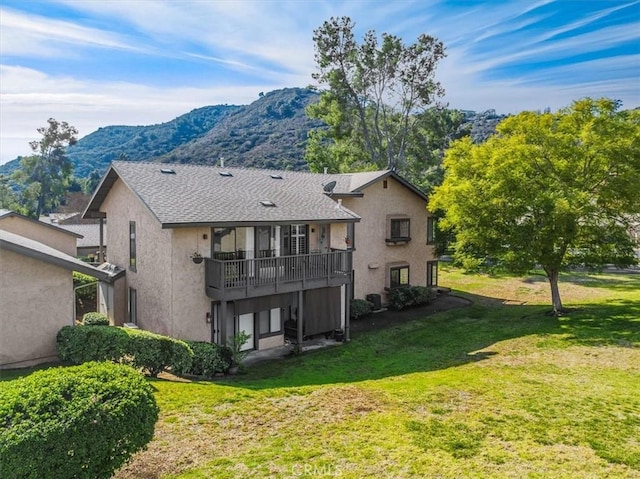 back of property with a shingled roof, a lawn, a balcony, a mountain view, and stucco siding