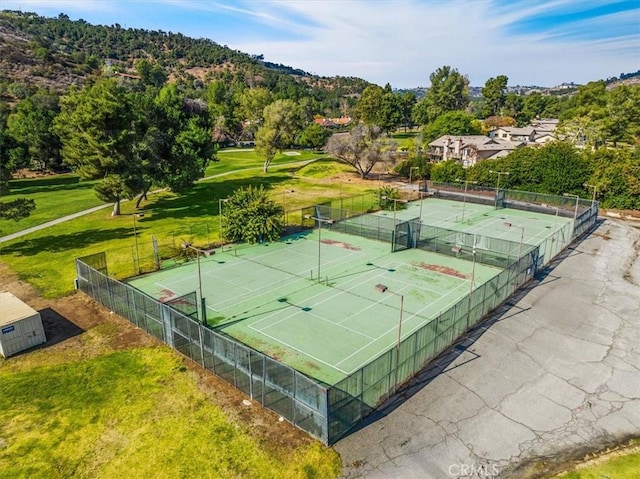 view of tennis court with a lawn and fence