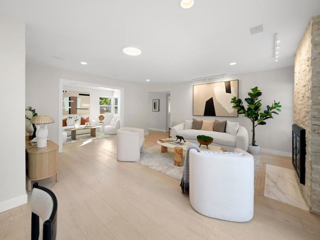 living room with a stone fireplace and light wood-type flooring