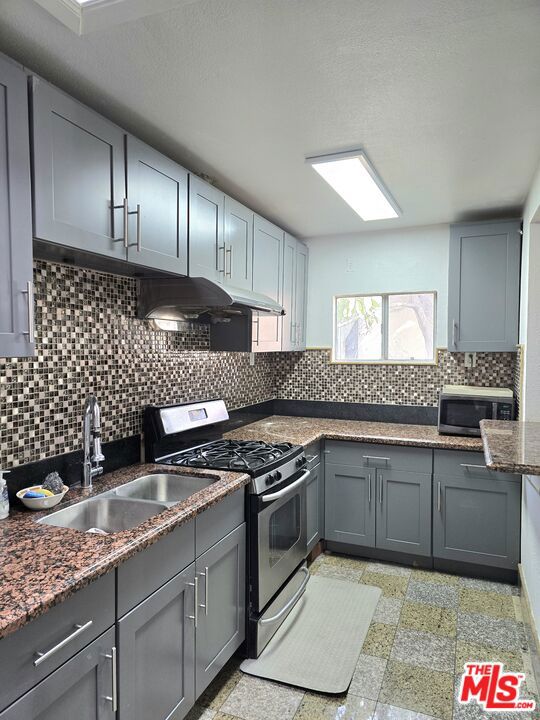 kitchen with sink, gray cabinets, appliances with stainless steel finishes, backsplash, and dark stone counters