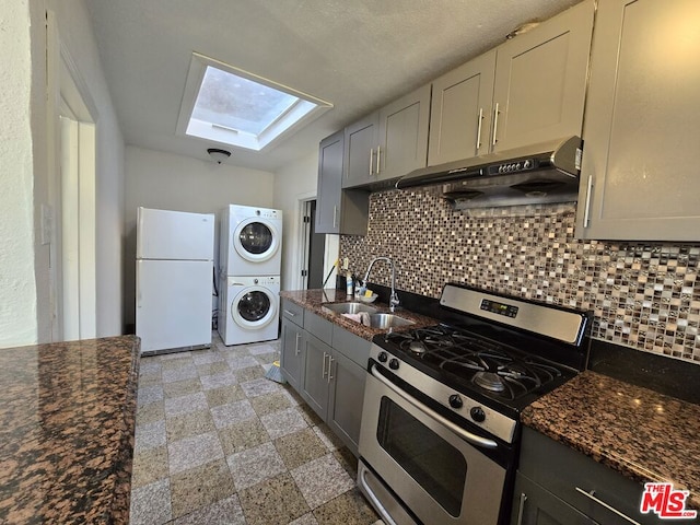 kitchen featuring sink, a skylight, stacked washer and clothes dryer, gas range, and white fridge