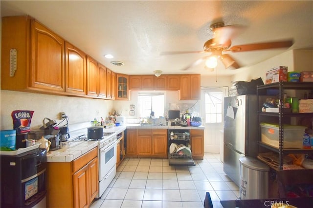 kitchen with white range with gas cooktop, tile counters, ceiling fan, and light tile patterned floors