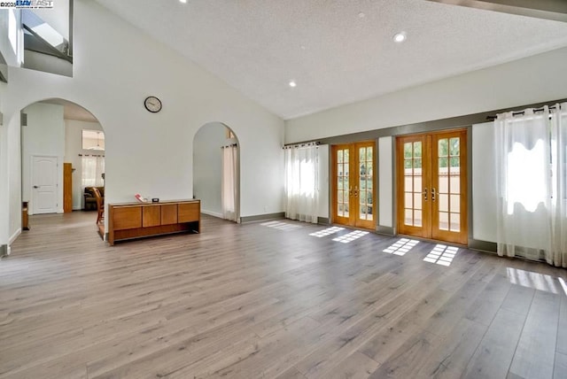 interior space with french doors, high vaulted ceiling, a textured ceiling, and light wood-type flooring