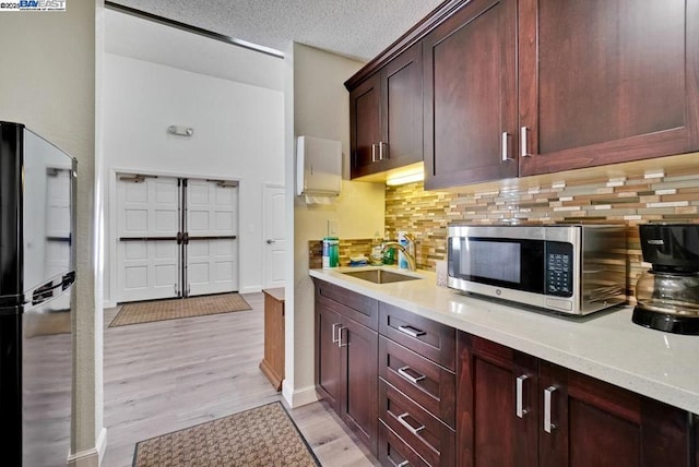 kitchen featuring sink, backsplash, light hardwood / wood-style floors, a textured ceiling, and black fridge