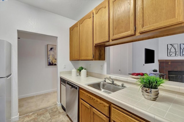 kitchen featuring sink, fridge, tile counters, dishwasher, and a fireplace