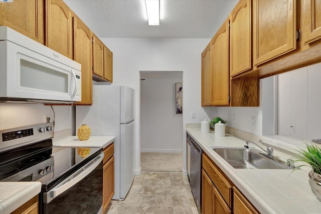 kitchen with stainless steel appliances, sink, tile countertops, and a textured ceiling