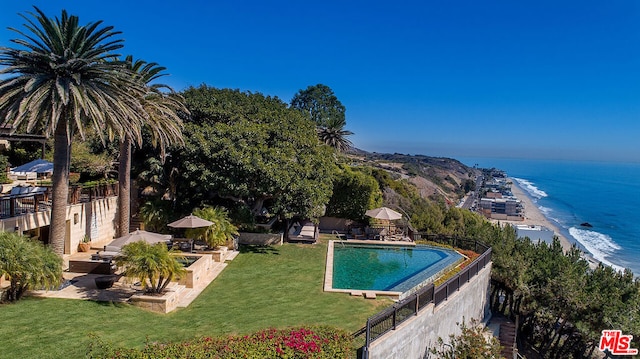 view of swimming pool with a water view, a yard, a view of the beach, and a grill