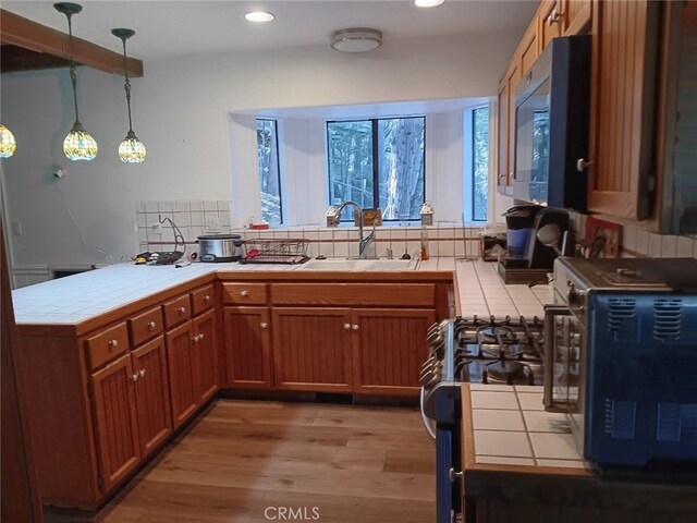 kitchen with sink, decorative light fixtures, tile countertops, kitchen peninsula, and light wood-type flooring