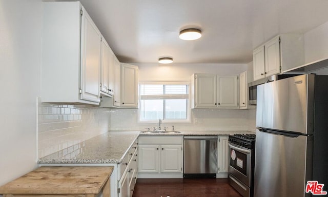 kitchen with sink, appliances with stainless steel finishes, white cabinets, light stone countertops, and backsplash