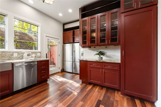 kitchen with light stone counters, stainless steel appliances, dark wood-type flooring, and backsplash