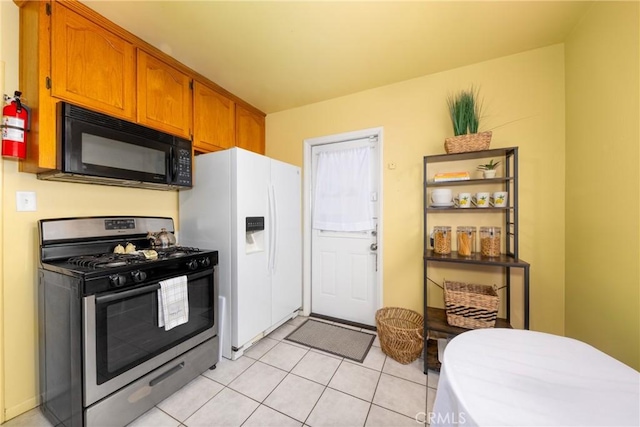 kitchen with stainless steel range with gas stovetop, light tile patterned floors, and white fridge with ice dispenser