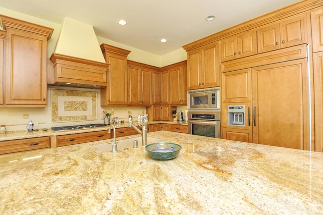 kitchen featuring custom exhaust hood, light stone countertops, sink, and built in appliances