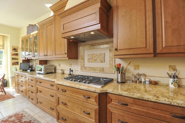 kitchen featuring light tile patterned floors, light stone countertops, custom range hood, and stainless steel gas stovetop