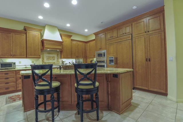 kitchen with premium range hood, a breakfast bar, built in appliances, a center island, and light stone countertops