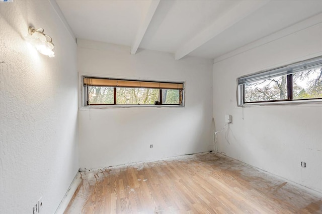 unfurnished room with beamed ceiling and light wood-type flooring