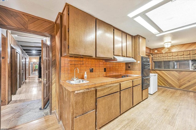 kitchen featuring tasteful backsplash, sink, light hardwood / wood-style floors, and wood walls