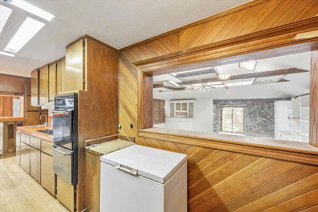 kitchen with light hardwood / wood-style flooring, refrigerator, black double oven, kitchen peninsula, and wood walls