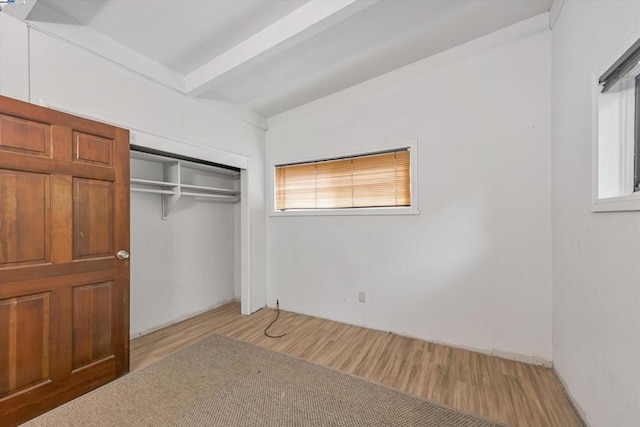 unfurnished bedroom with light hardwood / wood-style floors, a closet, and vaulted ceiling with beams