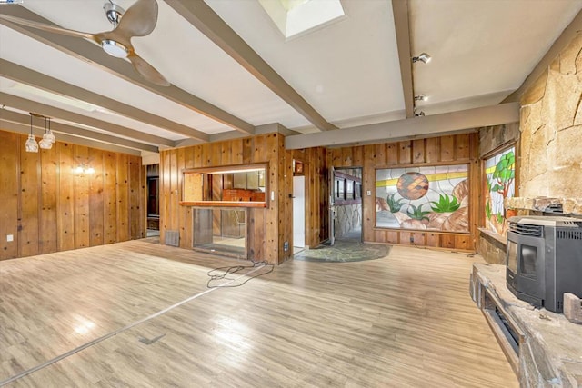 unfurnished living room with beam ceiling, light hardwood / wood-style flooring, wooden walls, and a wood stove