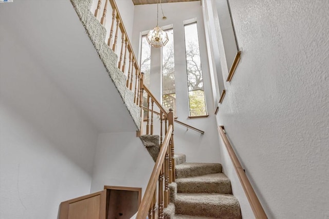 staircase with plenty of natural light, a towering ceiling, and a chandelier