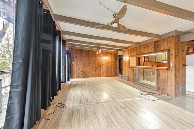 unfurnished living room featuring beamed ceiling, ceiling fan, wooden walls, and light hardwood / wood-style flooring