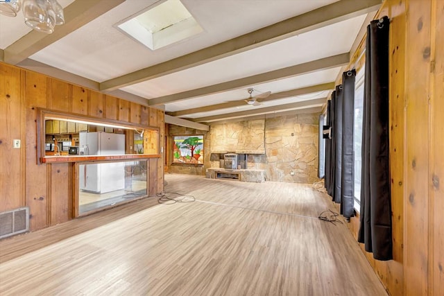 unfurnished living room with wood walls, a skylight, light hardwood / wood-style flooring, beamed ceiling, and a fireplace