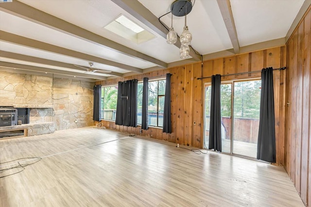 unfurnished living room featuring beamed ceiling, a healthy amount of sunlight, wooden walls, and light hardwood / wood-style flooring