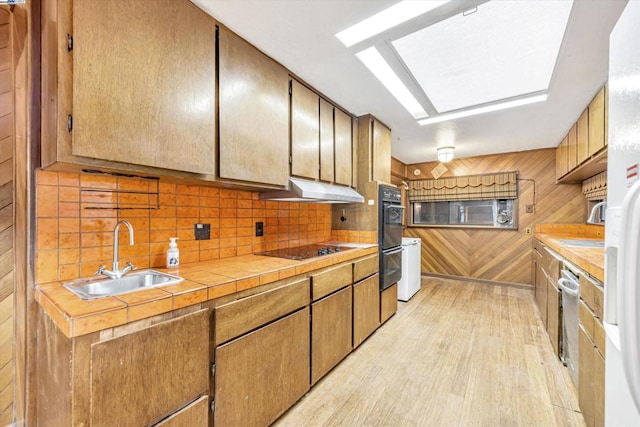 kitchen with wood walls, sink, backsplash, black electric stovetop, and light hardwood / wood-style floors