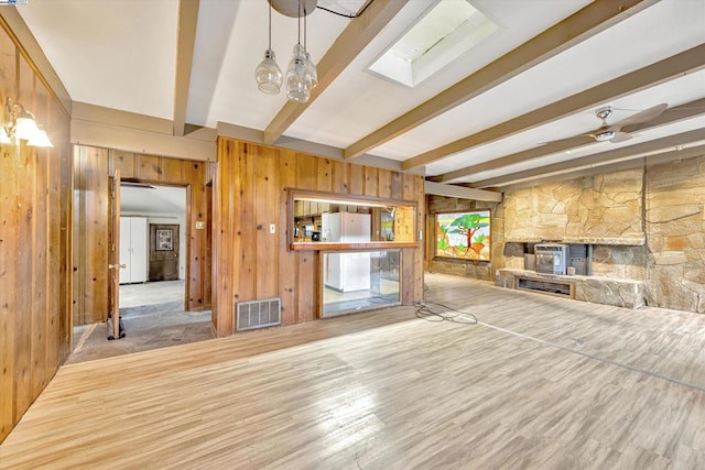 unfurnished living room featuring beam ceiling, a skylight, light wood-type flooring, wooden walls, and a fireplace