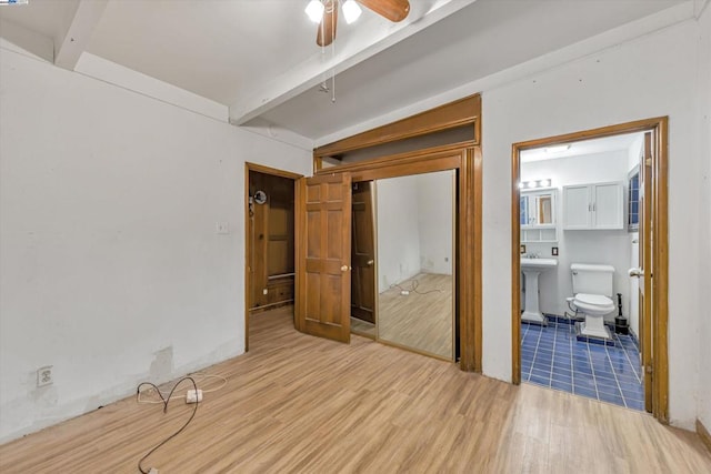 unfurnished bedroom with ensuite bathroom, lofted ceiling with beams, sink, light wood-type flooring, and a closet