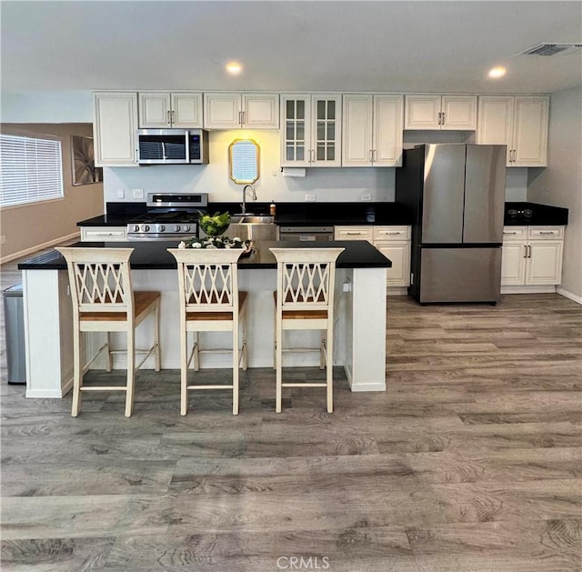 kitchen with sink, a kitchen breakfast bar, stainless steel appliances, hardwood / wood-style floors, and white cabinets