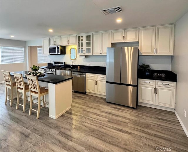 kitchen with a breakfast bar area, white cabinetry, stainless steel appliances, a kitchen island, and light wood-type flooring