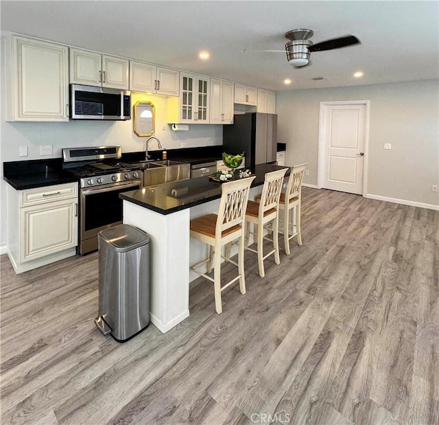 kitchen featuring a breakfast bar, appliances with stainless steel finishes, white cabinetry, a center island, and light wood-type flooring