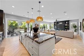 kitchen with white cabinets, dark stone counters, hanging light fixtures, light parquet floors, and a spacious island