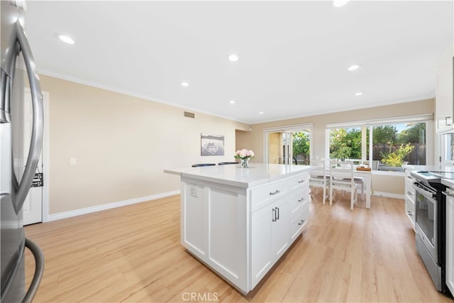 kitchen with light hardwood / wood-style flooring, white cabinetry, stainless steel appliances, ornamental molding, and a kitchen island