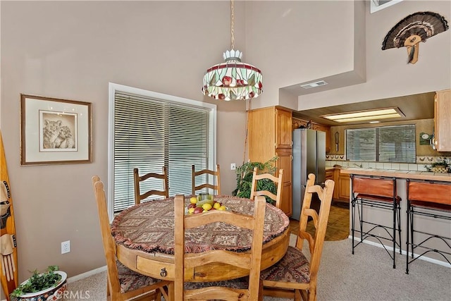 dining space featuring light colored carpet and a high ceiling