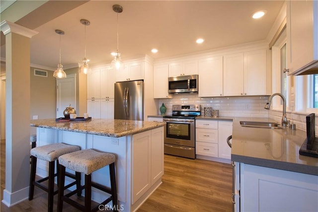 kitchen featuring sink, decorative light fixtures, appliances with stainless steel finishes, a kitchen island, and white cabinets