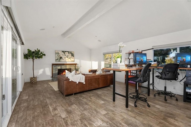 office area featuring vaulted ceiling with beams, a lit fireplace, baseboards, and wood finished floors