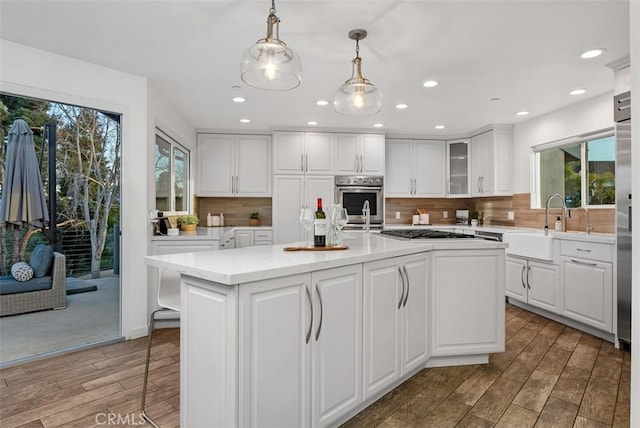 kitchen featuring stainless steel gas stovetop, white cabinetry, backsplash, and wood finished floors