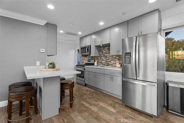 kitchen featuring a breakfast bar area, dark wood-type flooring, a sink, appliances with stainless steel finishes, and gray cabinets