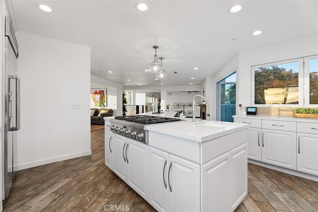 kitchen with open floor plan, a kitchen island with sink, stainless steel gas cooktop, and wood finished floors