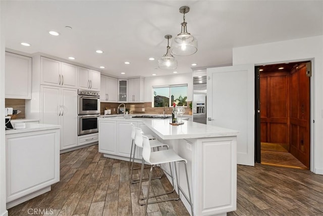 kitchen featuring dark wood-style floors, a center island with sink, stainless steel appliances, light countertops, and white cabinetry