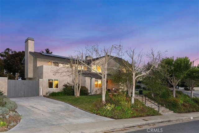 view of front of house with solar panels, driveway, a gate, stucco siding, and a front yard