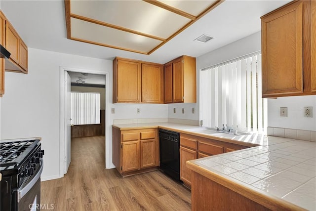 kitchen featuring sink, tile counters, black appliances, kitchen peninsula, and light wood-type flooring