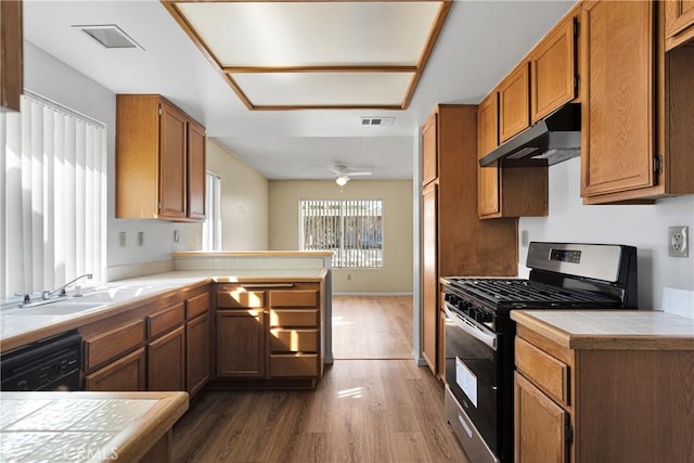 kitchen featuring stainless steel range with gas cooktop, dishwasher, dark hardwood / wood-style flooring, tile counters, and kitchen peninsula