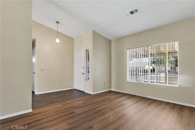 spare room with vaulted ceiling, dark hardwood / wood-style floors, and a textured ceiling